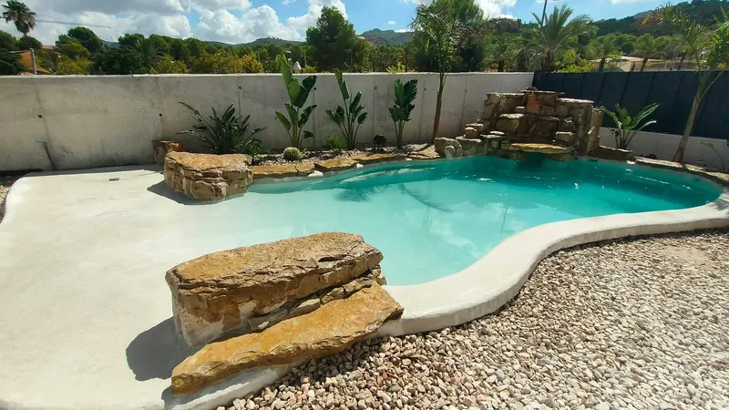 Piscina de arena con cascada de piedra y vegetación